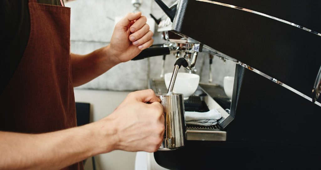 Selvstændig barista bruger mælkesteamer i kaffebar